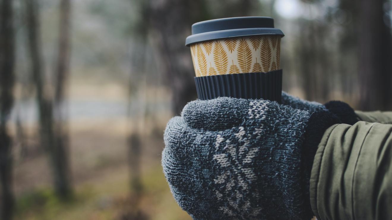 someone wearing mittens holding a travel mug outside