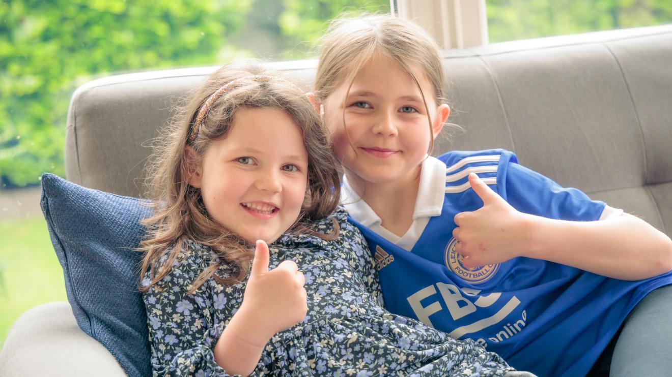 two children sitting on sofa giving thumbs up
