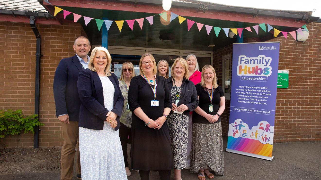 Group of people standing outside a family hub next to a family hub pull-up banner 