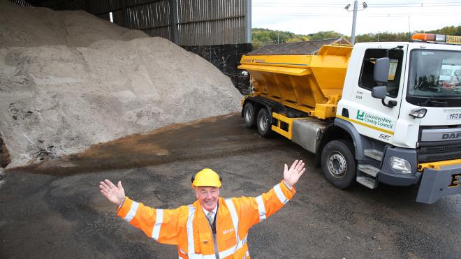 Man in highvis and helmet infront of a gritting lorry and a big pile of gritting salt