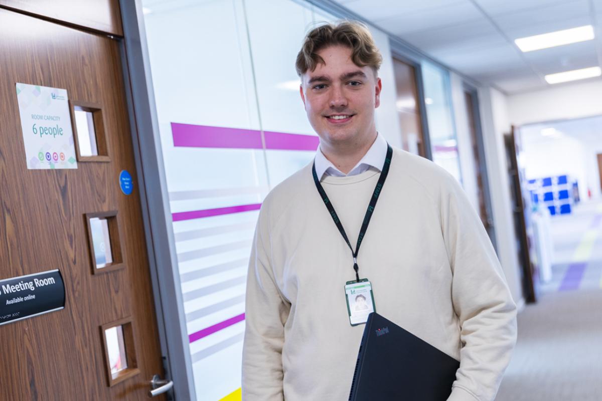 One our apprentices holding a laptop and standing outside a meeting room